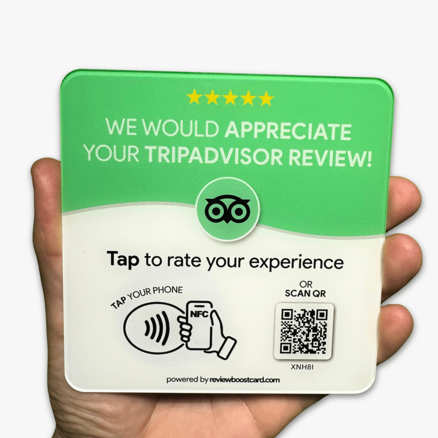 A hand holding a green plaque that reads "WE WOULD APPRECIATE YOUR TRIPADVISOR REVIEW!" at the top with five stars above the text. Below is the TripAdvisor logo, and further down, the text says "Tap to rate your experience" with an illustration of a phone tapping an NFC symbol. There is also a QR code on the right side for an alternative way to rate the experience. The bottom of the plaque reads "powered by reviewboostcard.com